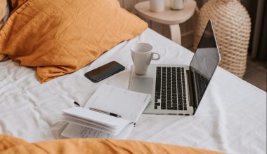 laptop-with-copybook-and-cup-of-coffee-on-bed-sheet