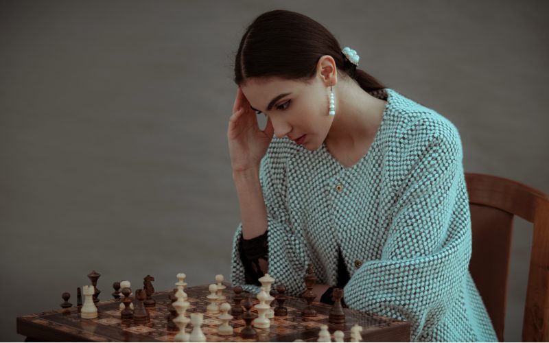 wanita yang sedang memikirkan pergerakan bidak catur